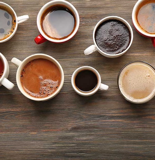 lots of coffee in cups and mugs of different shapes and colors on a wood table
