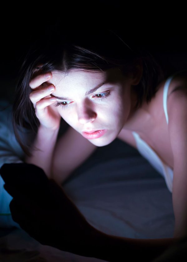 teenage girl in bed at night looking stressed at tragic news about the Texas flooding that she is reading on her mobile phone