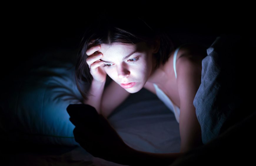 teenage girl in bed at night looking stressed at tragic news about the Texas flooding that she is reading on her mobile phone