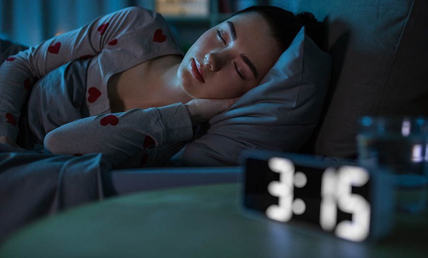 teenage girl sleeping in bed next to alarm clock showing 3:15 a.m.