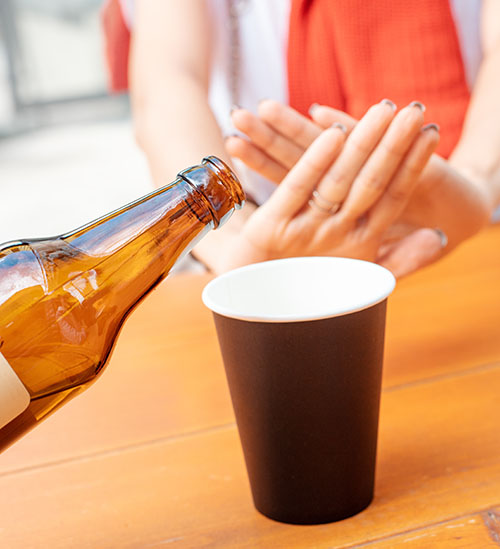 womans hands showing her refusing alcohol while another person starts to pour beer into a cup