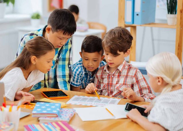 five elementary school children at a table working on math class homework