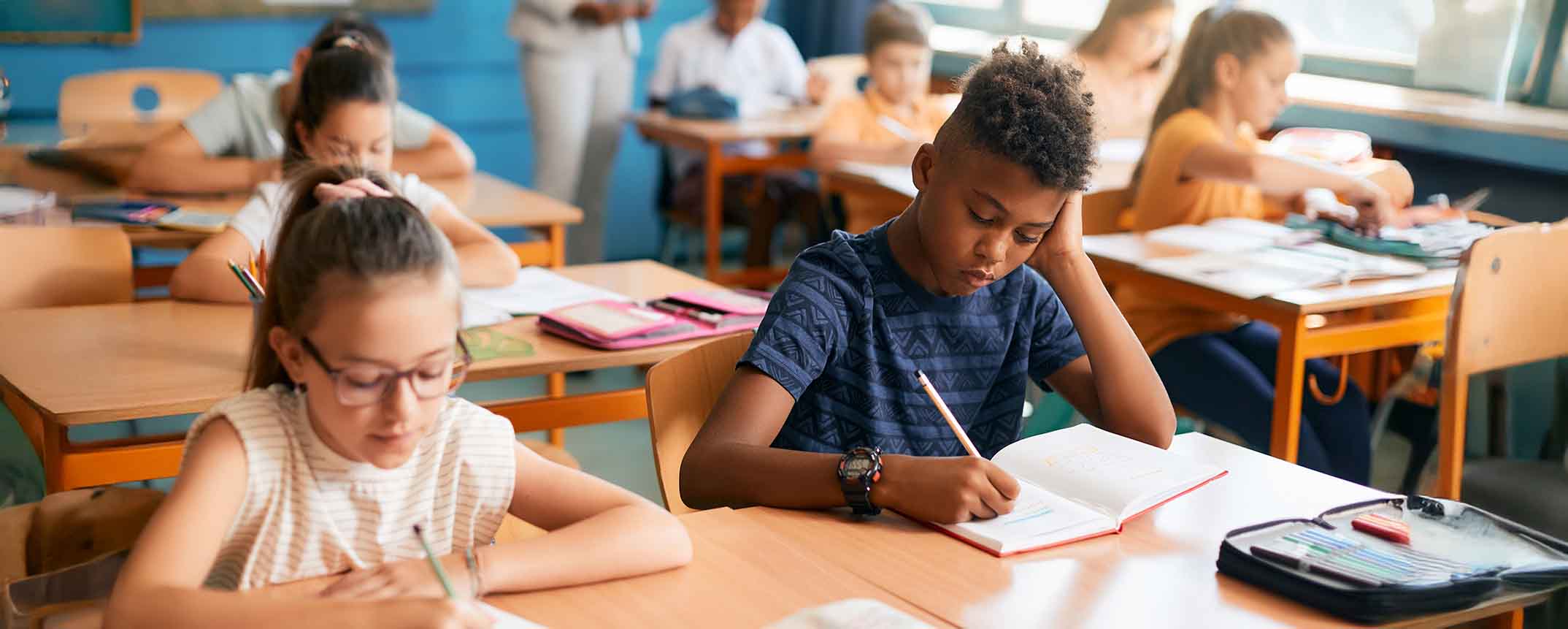 middle school students at desks in classroom writing in notebooks