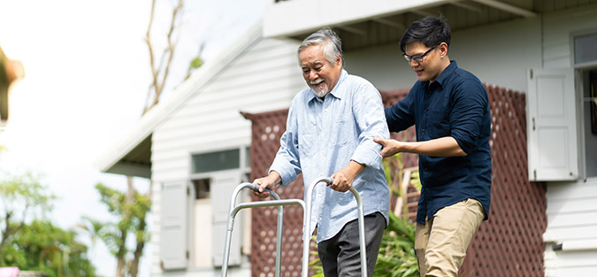 Elderly Asian father and Adult son walking in backyard, example of caregiving stress many workers face