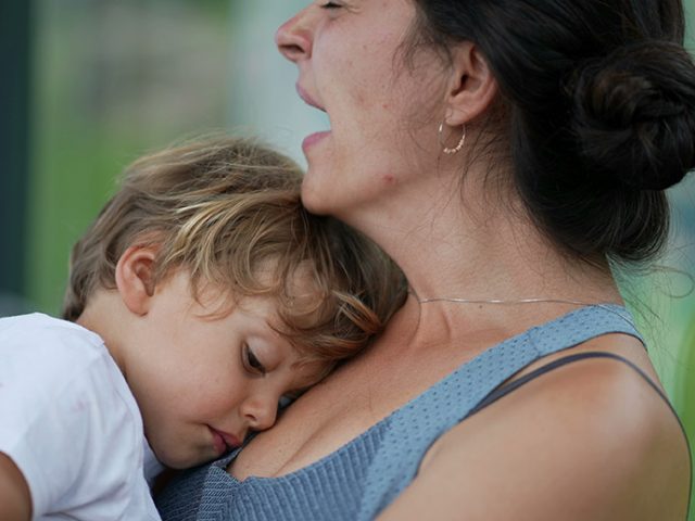 tired mom holding sleeping toddler stressed with childcare costs