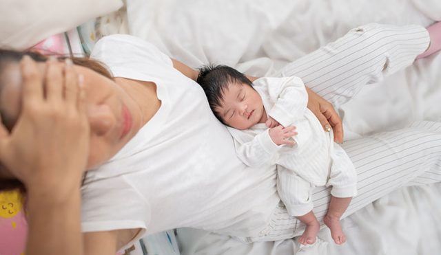 tired mother suffering from postnatal depression sitting on bed holding her sleeping baby, parenting stress
