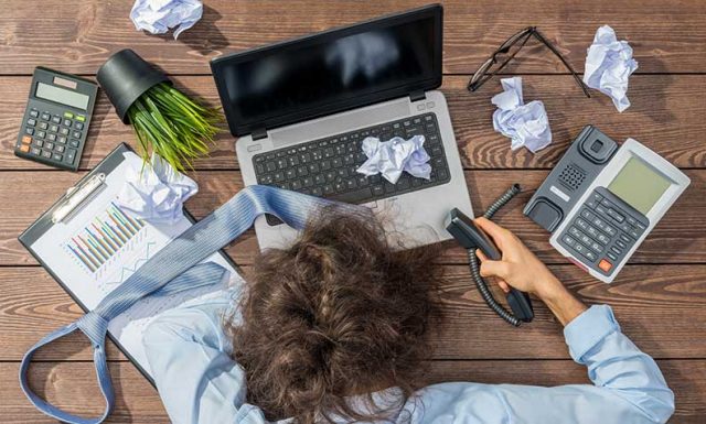 person stressed at work with mess around their desk, laptop and phone