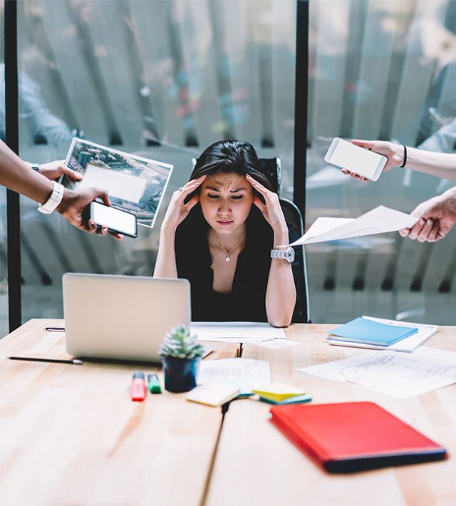 woman at work with too much to do and people handing her more things to handle