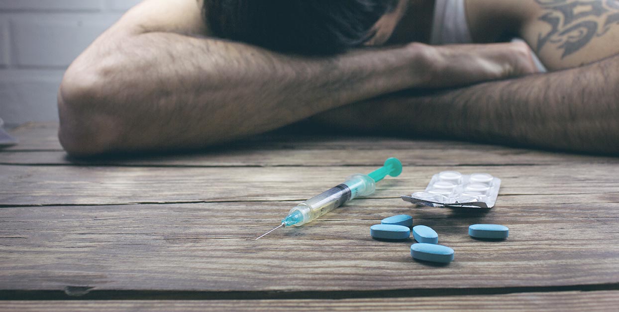 drugs in pills and syringe with man who is addicted and depressed