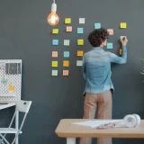 A woman organizing colorful post its on a wall.
